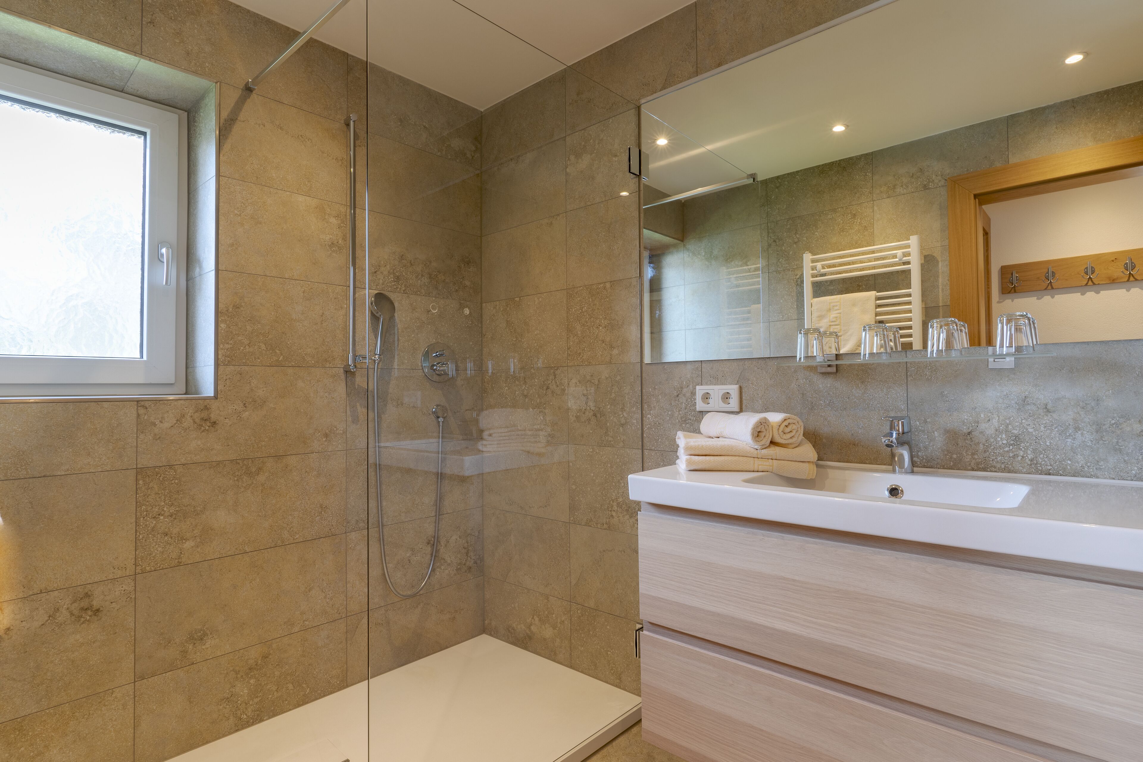 A modern bathroom with a glass-enclosed shower, a large mirror, and a white sink with a wooden vanity.