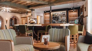 A cozy bar area with wooden beams, striped upholstered chairs, and a round wooden table with a candle. - Hotel Piz Buin (Ischgl)