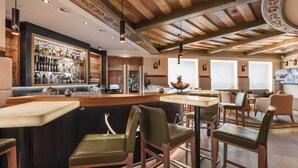 A bar area with wooden ceiling beams, bar stools, and a display of liquor bottles. - Hotel Piz Buin (Ischgl)