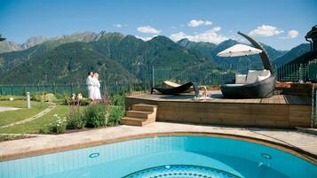 Ein Pool mit Bergblick, eine Holzterrasse und eine Lounge-Bereich mit Stuhl und Sonnenschirm.