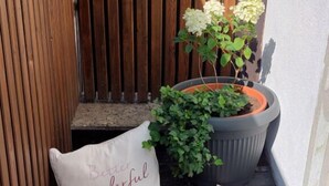 A small outdoor seating area with a wooden bench, a potted plant, and a cushion with text. - Haus Montana (Lermoos)