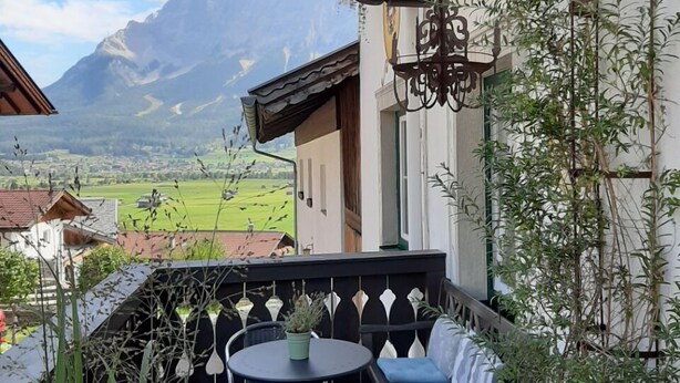 A wooden deck with a table and chairs, surrounded by potted plants and a view of a mountain landscape. - Haus Montana (Lermoos)
