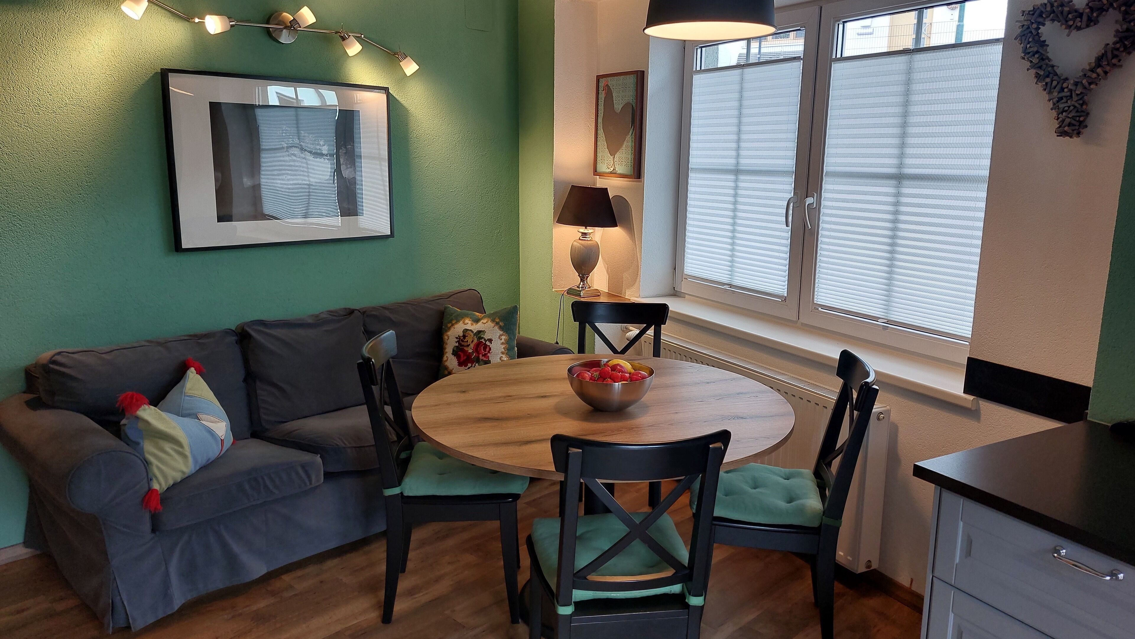 Una sala de estar acogedora con un sofá, sillas, una mesa de comedor con fruteros, una lámpara y una ventana con persianas.
