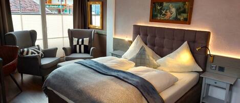 A hotel room with a large bed, two armchairs, a small table, and a painting on the wall.