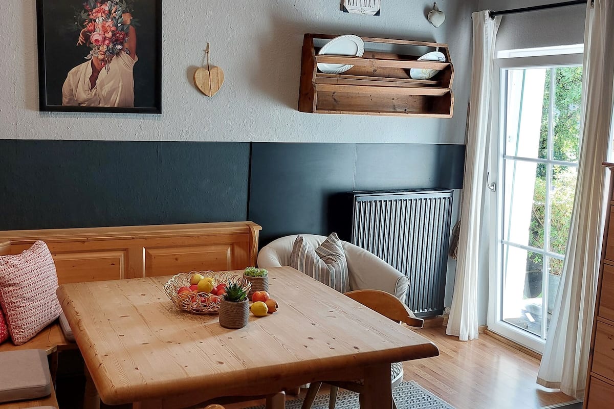 A cozy room with a wooden bench, a table with fruit, a radiator, and a window with curtains.