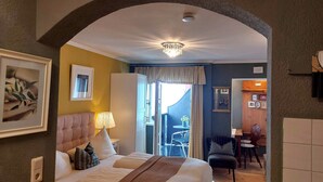 A hotel room with a bed, a nightstand, a lamp, a window with curtains, and a view of the dining area. - Haus Montana (Lermoos)