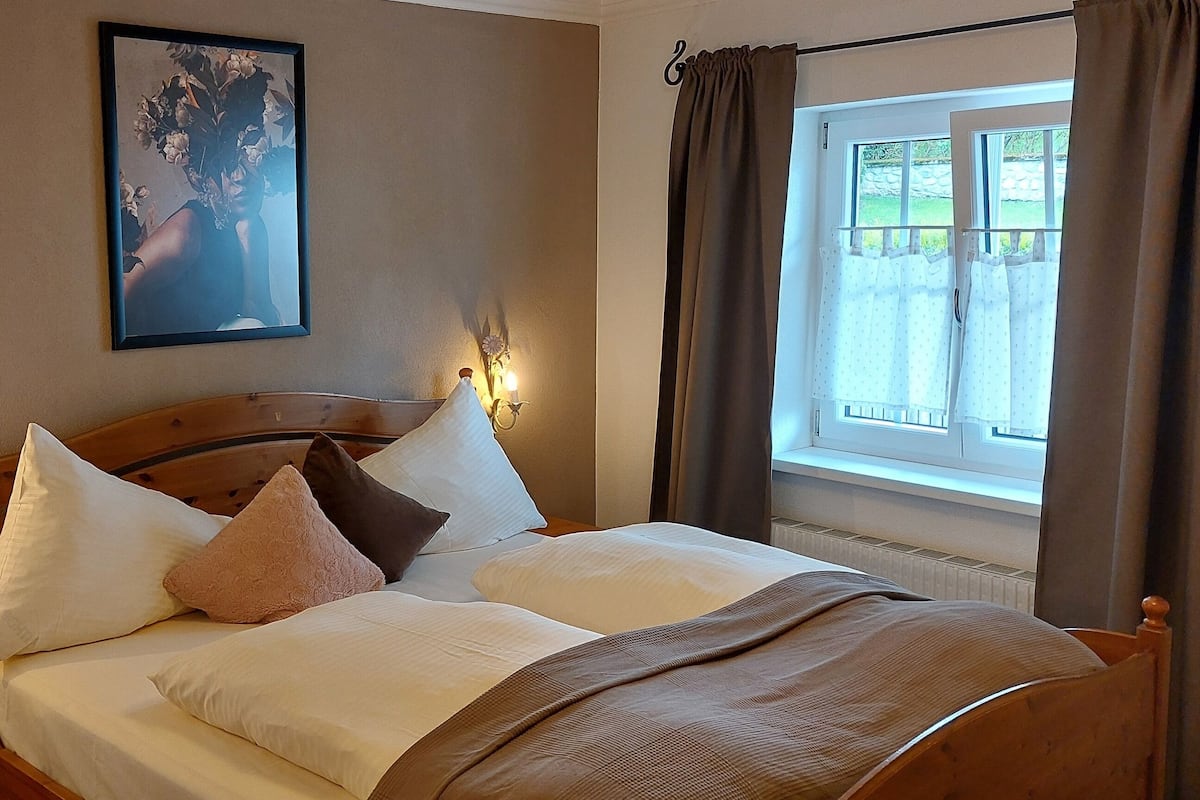 A neatly made bed with white and brown bedding, a wooden headboard, and a wall-mounted picture.