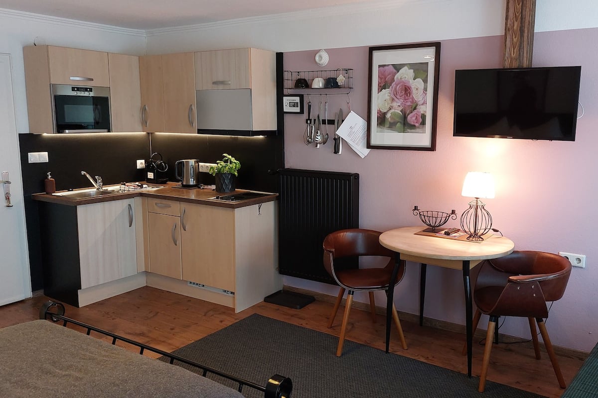 A compact kitchen with modern appliances, a dining area with two chairs, and a TV mounted on the wall.
