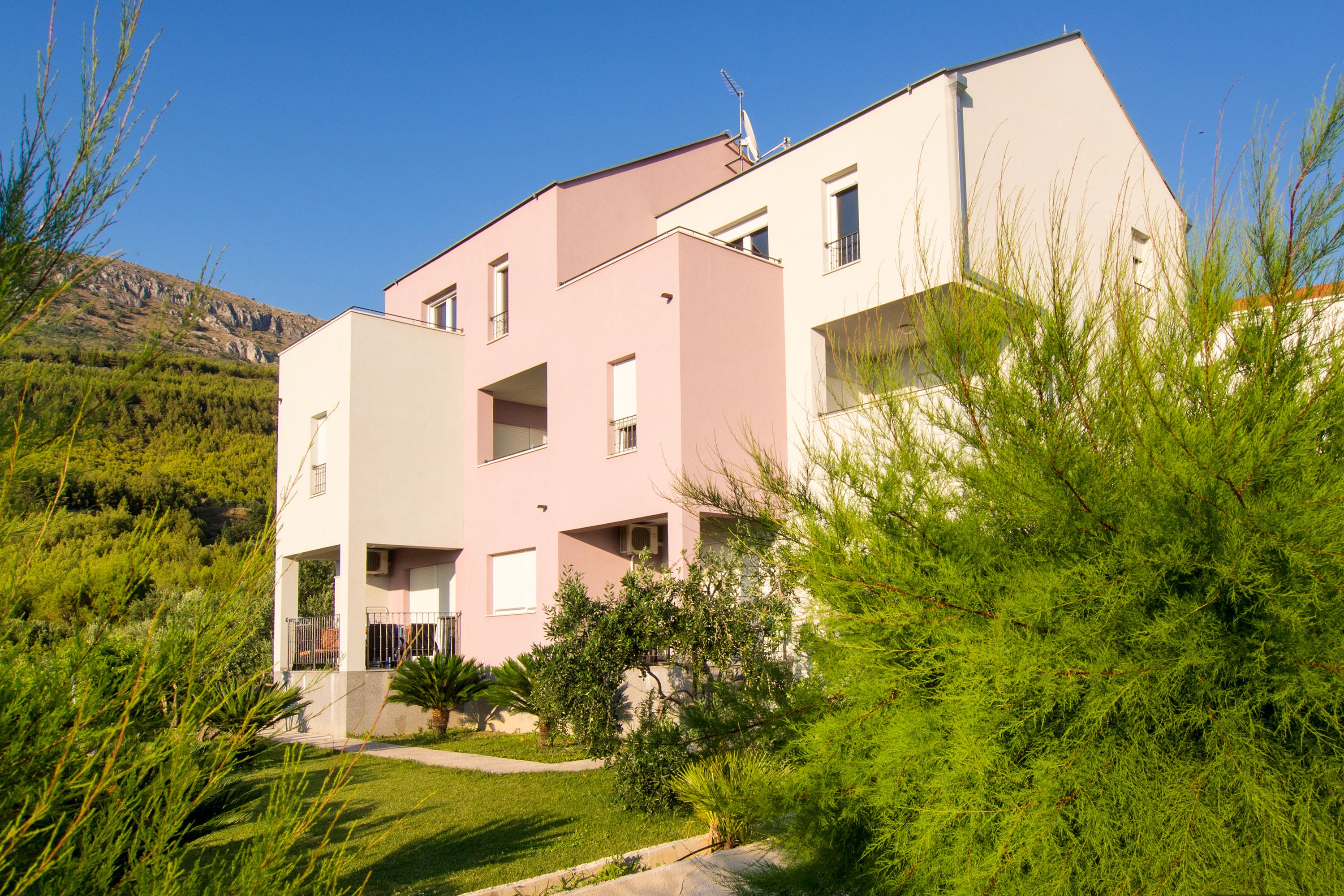 A modern two-story building with a flat roof, surrounded by greenery and a hillside in the background.