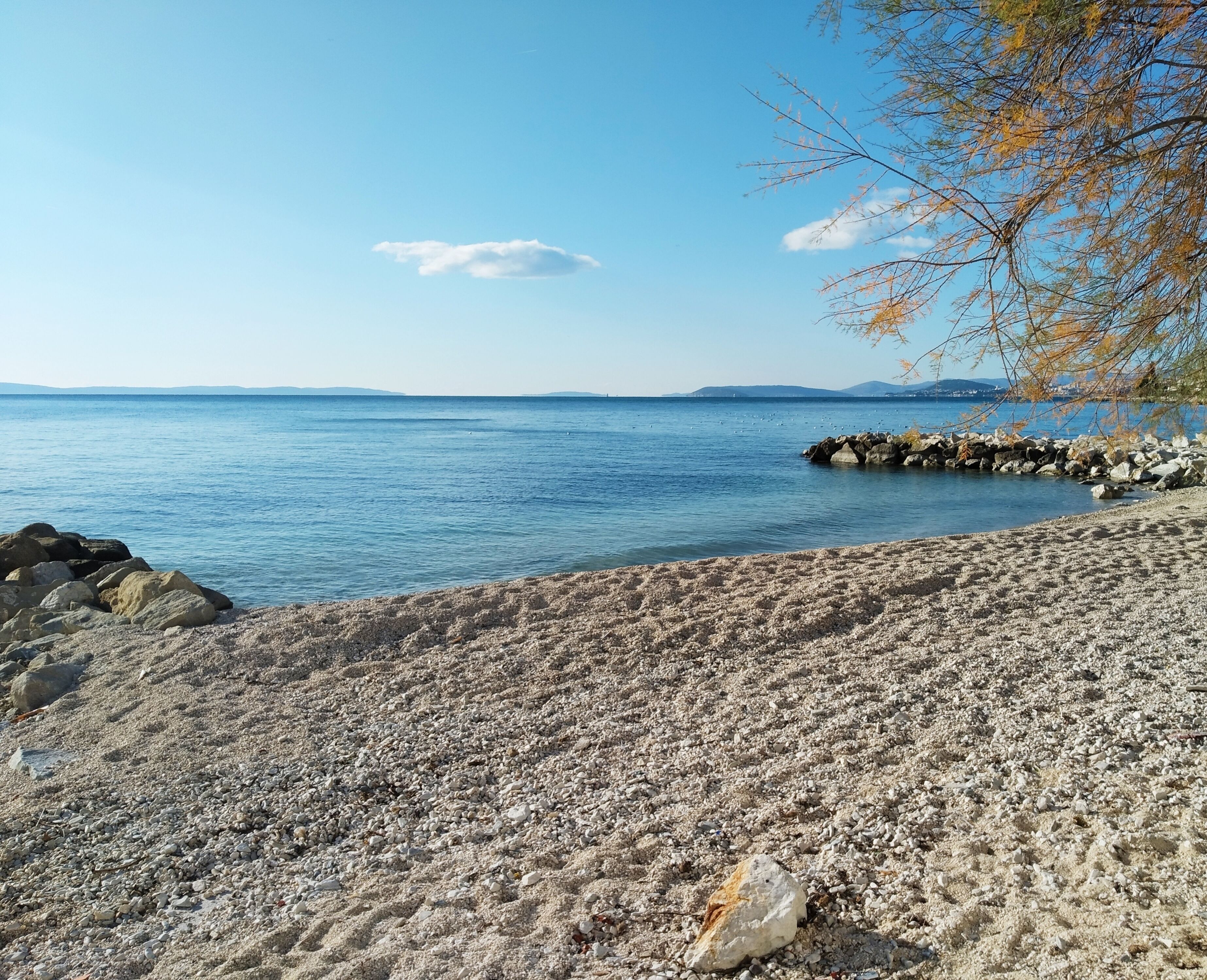 A pebble beach with a rocky shoreline and calm water.