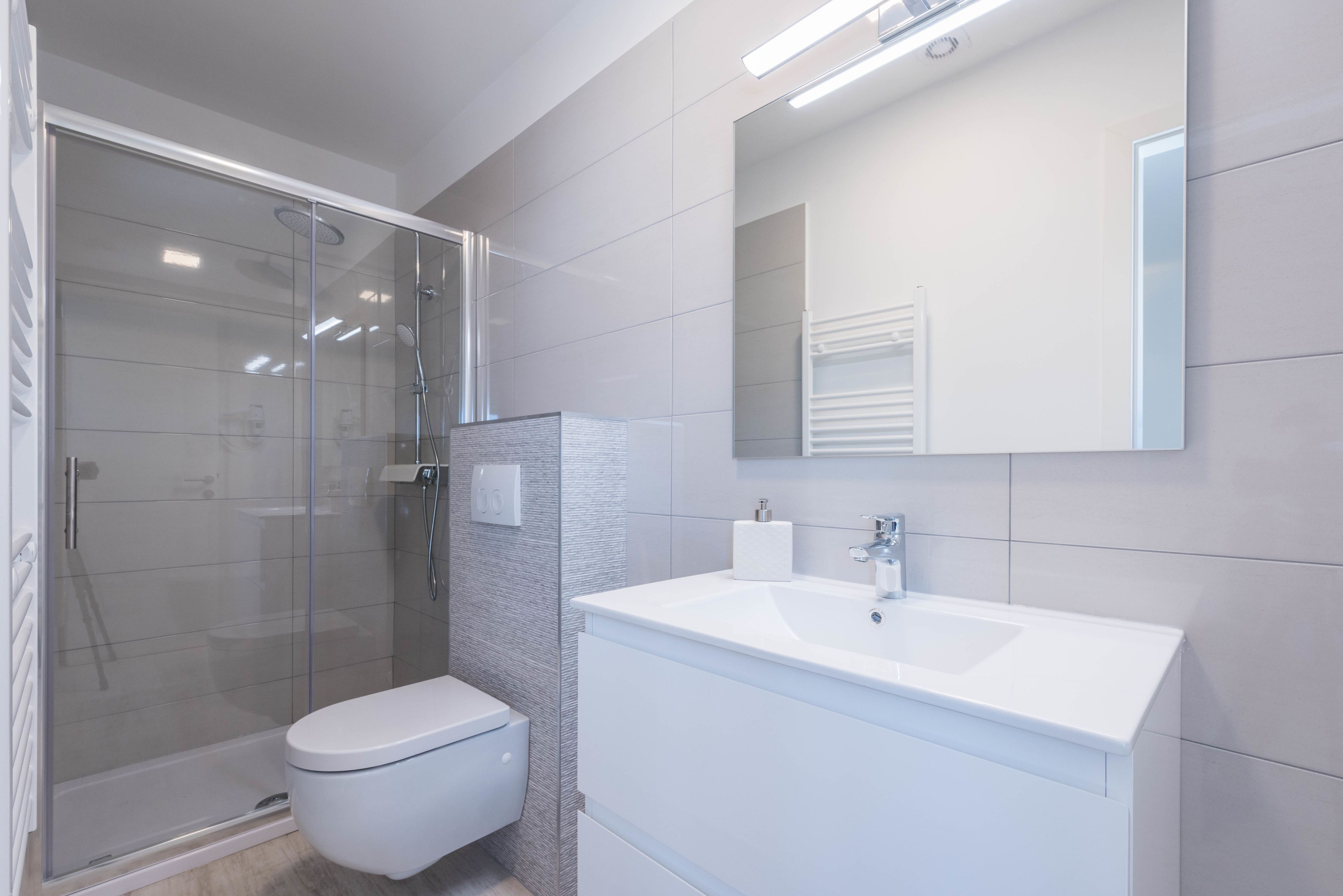 A modern bathroom with a glass-enclosed shower, a white toilet, and a white vanity with a mirror.