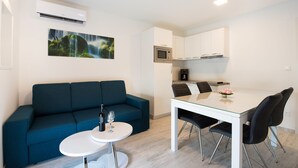 A modern living room with a blue sofa, a small round table with a bottle and glass, and a dining area with a white table and black chairs. - Villa Lavanda (Podstrana)