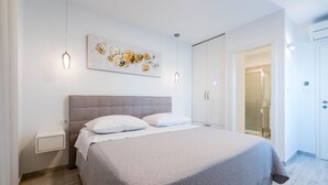A modern bedroom with a large bed, a nightstand, a wall-mounted artwork, and a door leading to a bathroom. - Villa Lavanda (Podstrana)