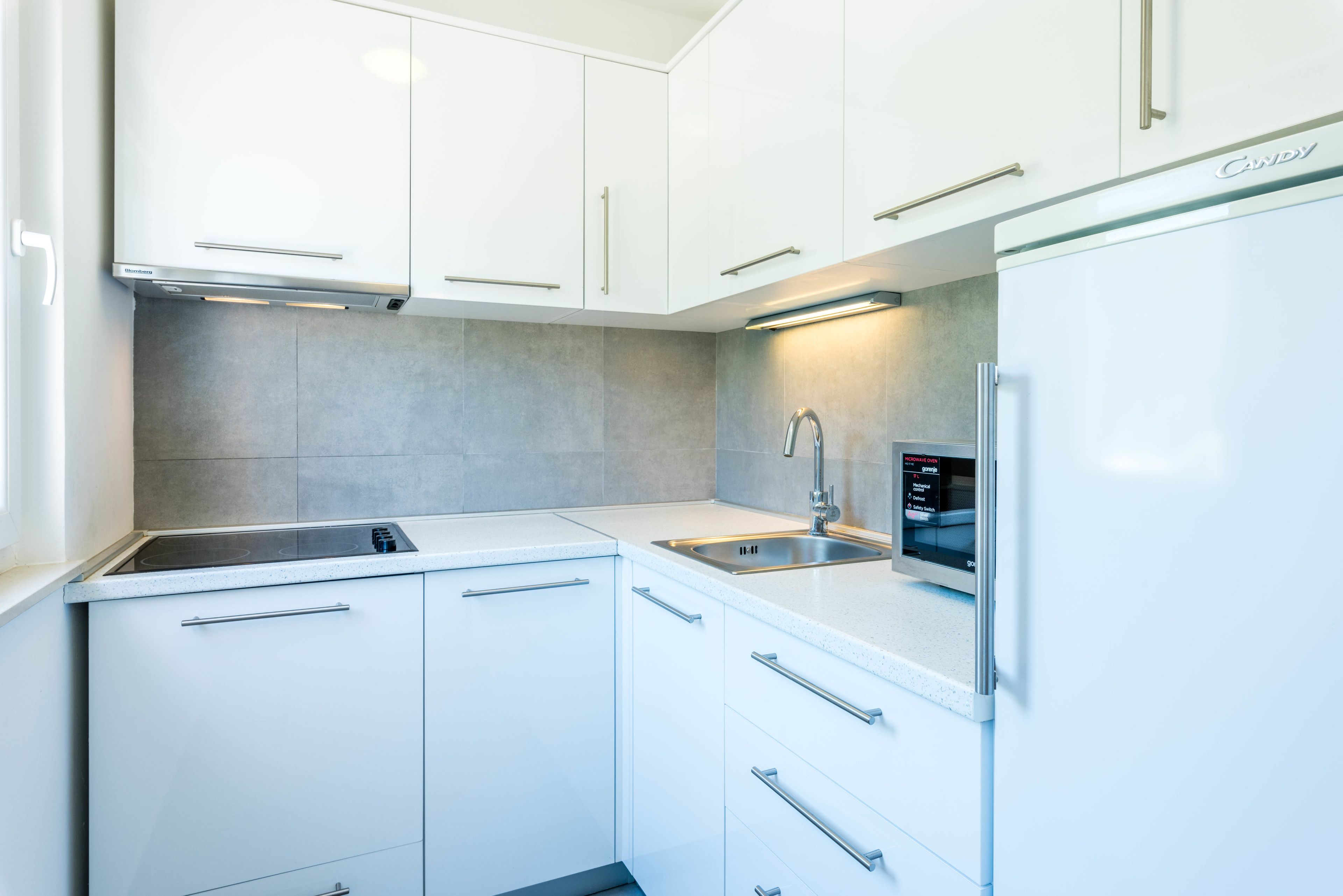 A modern kitchen with white cabinets, a stainless steel sink, and a built-in refrigerator.