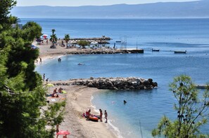 Una playa con aguas azules cristalinas, formaciones rocosas y algunos barcos.