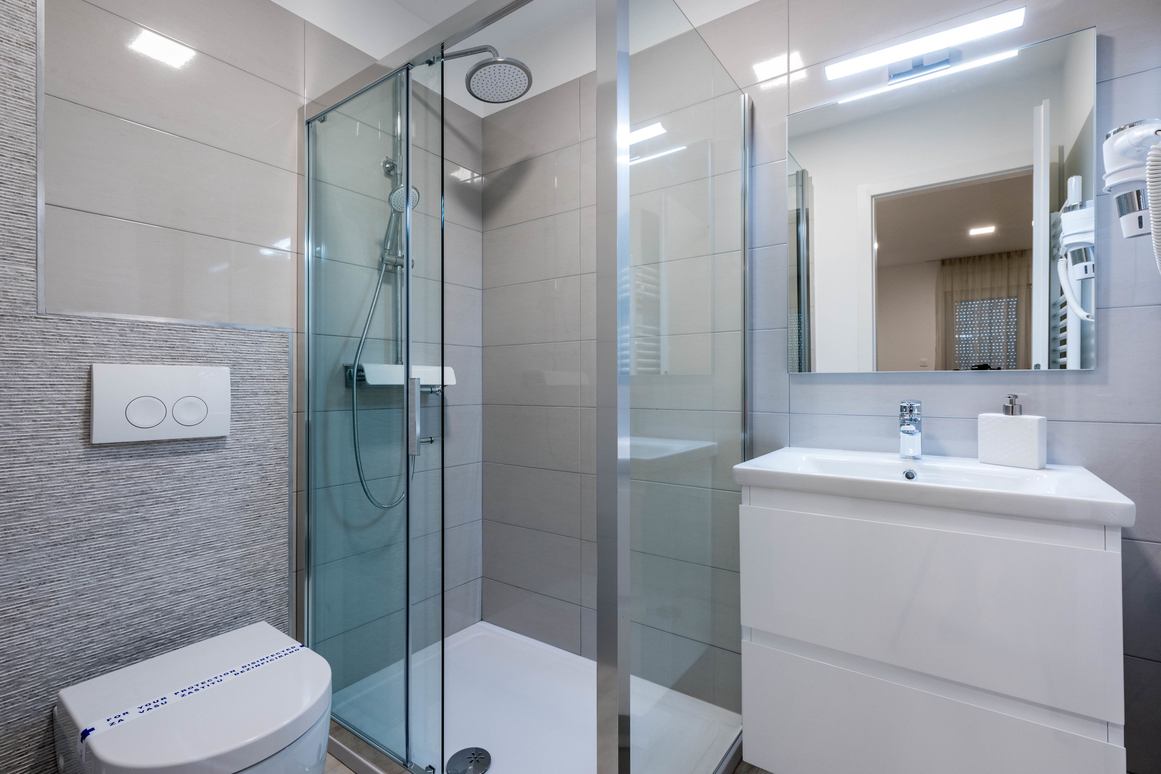 A modern bathroom with a glass-enclosed shower, a white toilet, and a sink with a mirror above it.