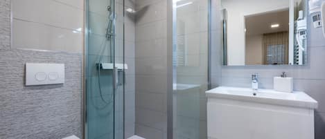 A modern bathroom with a glass-enclosed shower, a white toilet, and a sink with a mirror above it.