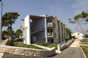 Un immeuble résidentiel à plusieurs étages, doté de balcons, d’un mur de soutènement en pierre et d’une allée pavée.
