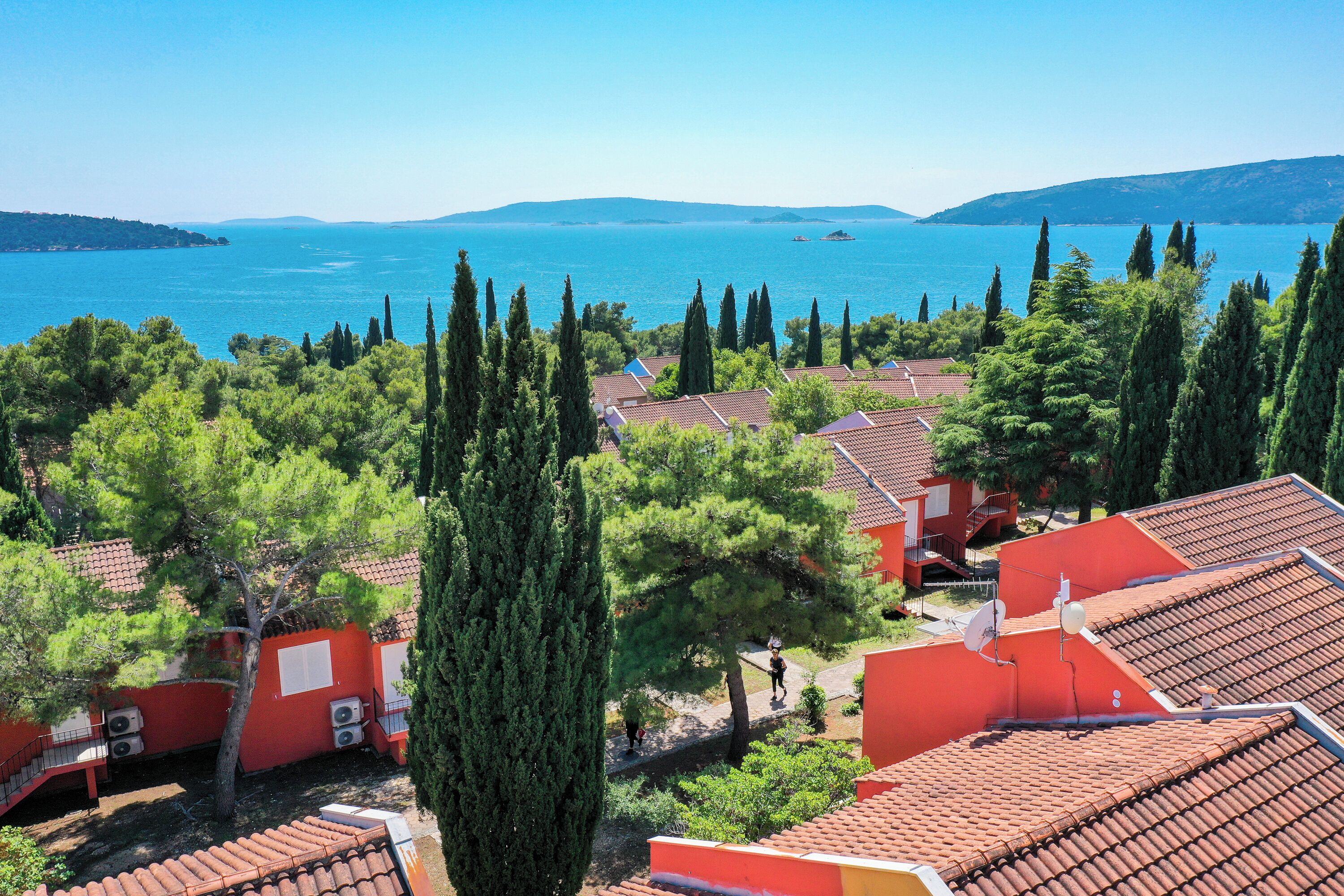 Un villaggio costiero con edifici a tetto di tegole, cipressi e vista sul mare.
