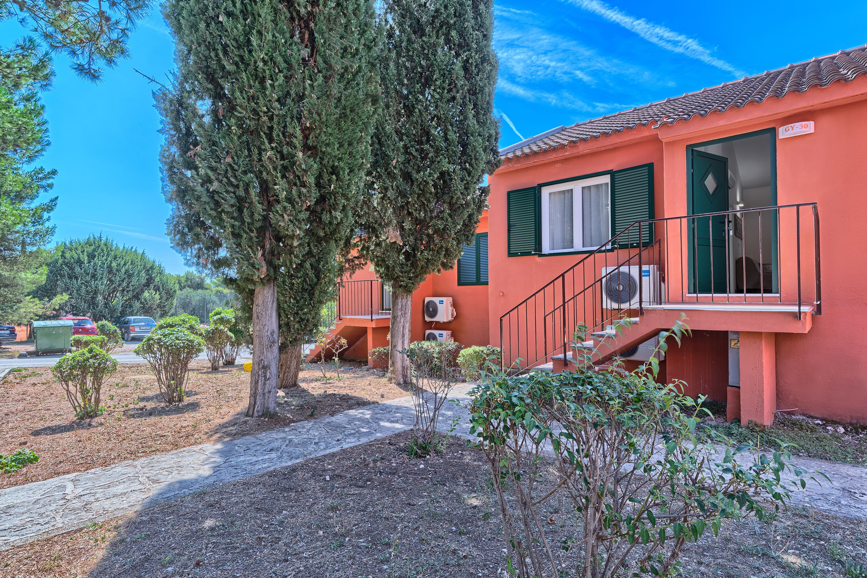 A red building with a staircase, green shutters, and a clear sky.