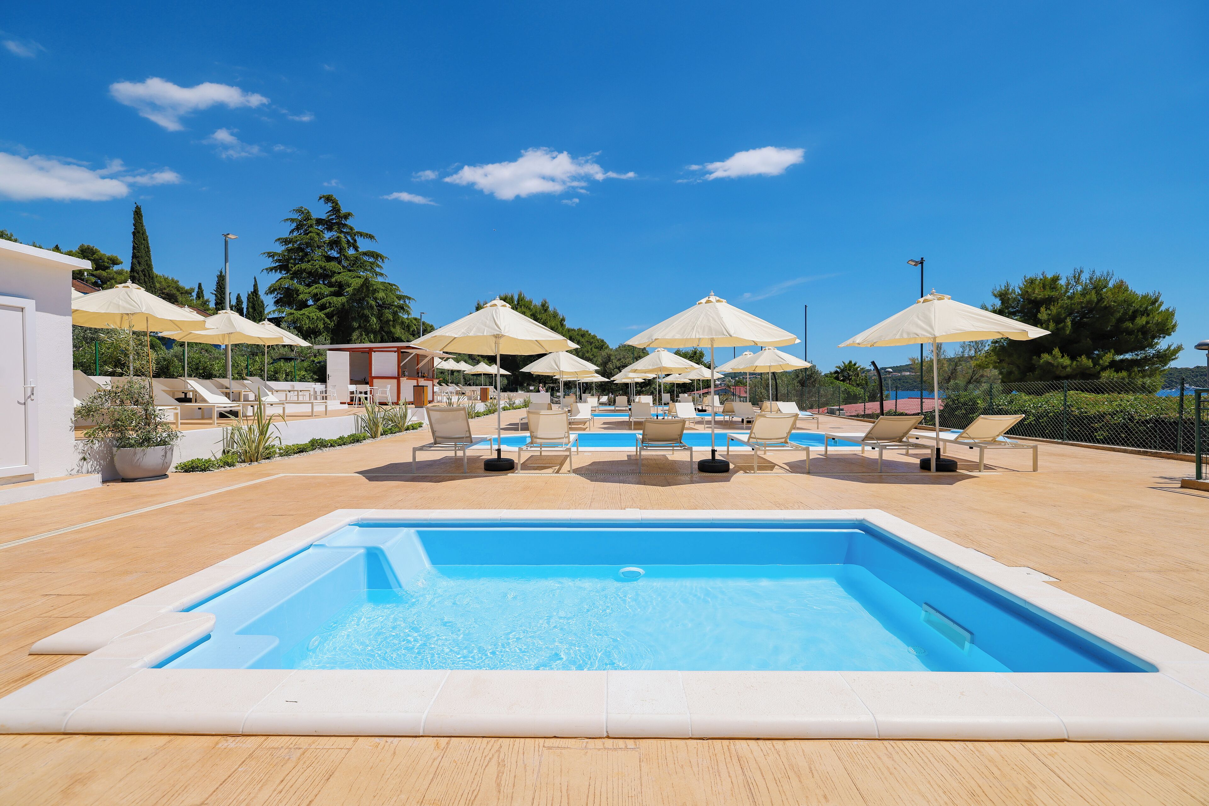 A rectangular swimming pool with lounge chairs and umbrellas around it.