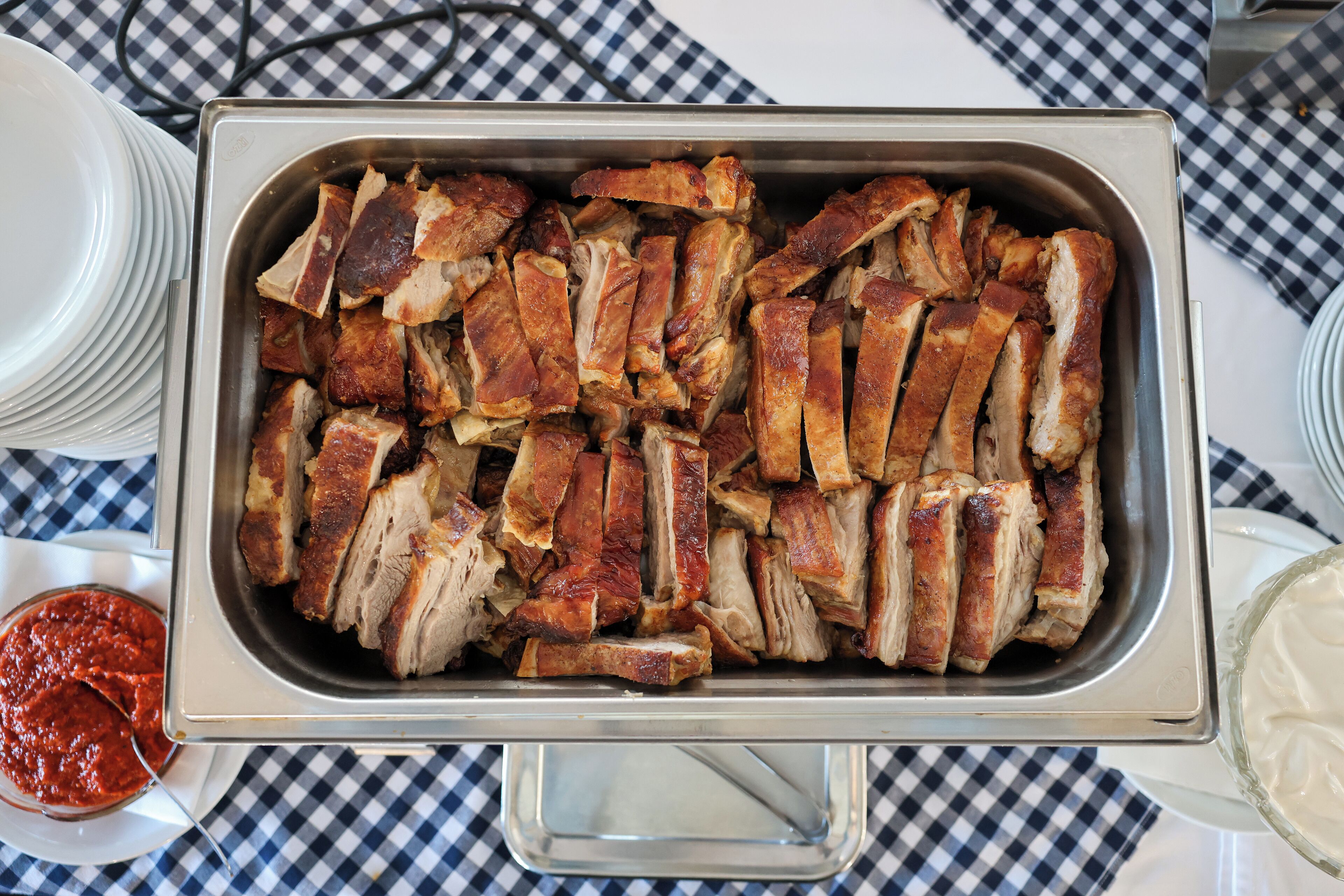 A buffet table with a tray of sliced meat, a bowl of sauce, and plates.
