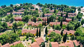 An aerial view of a coastal residential area with houses having red-tiled roofs, surrounded by greenery and trees, with a clear blue sea in the background. - Apartments Medena (Seget)