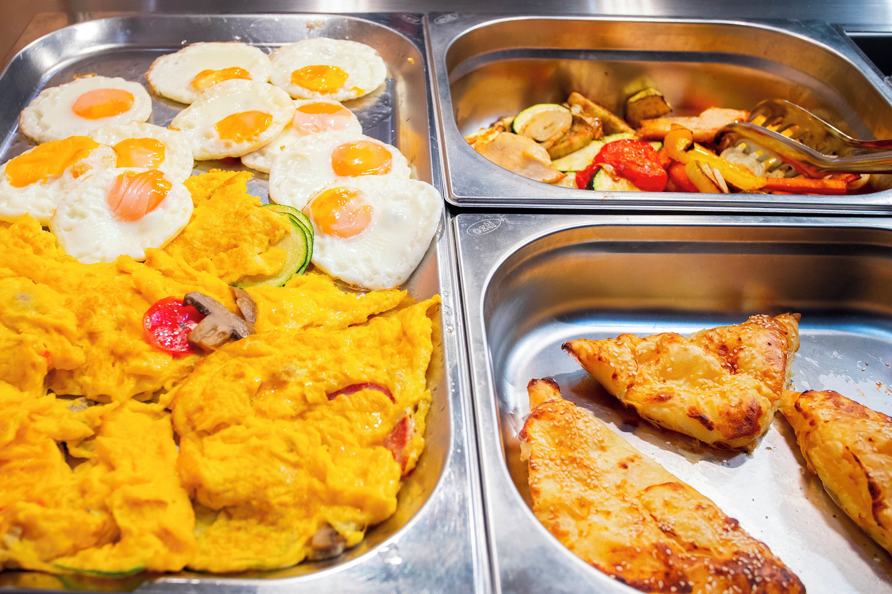 Ein Buffet mit verschiedenen Speisen, darunter Rührei, Spiegeleier und einer Auswahl an Gemüse.