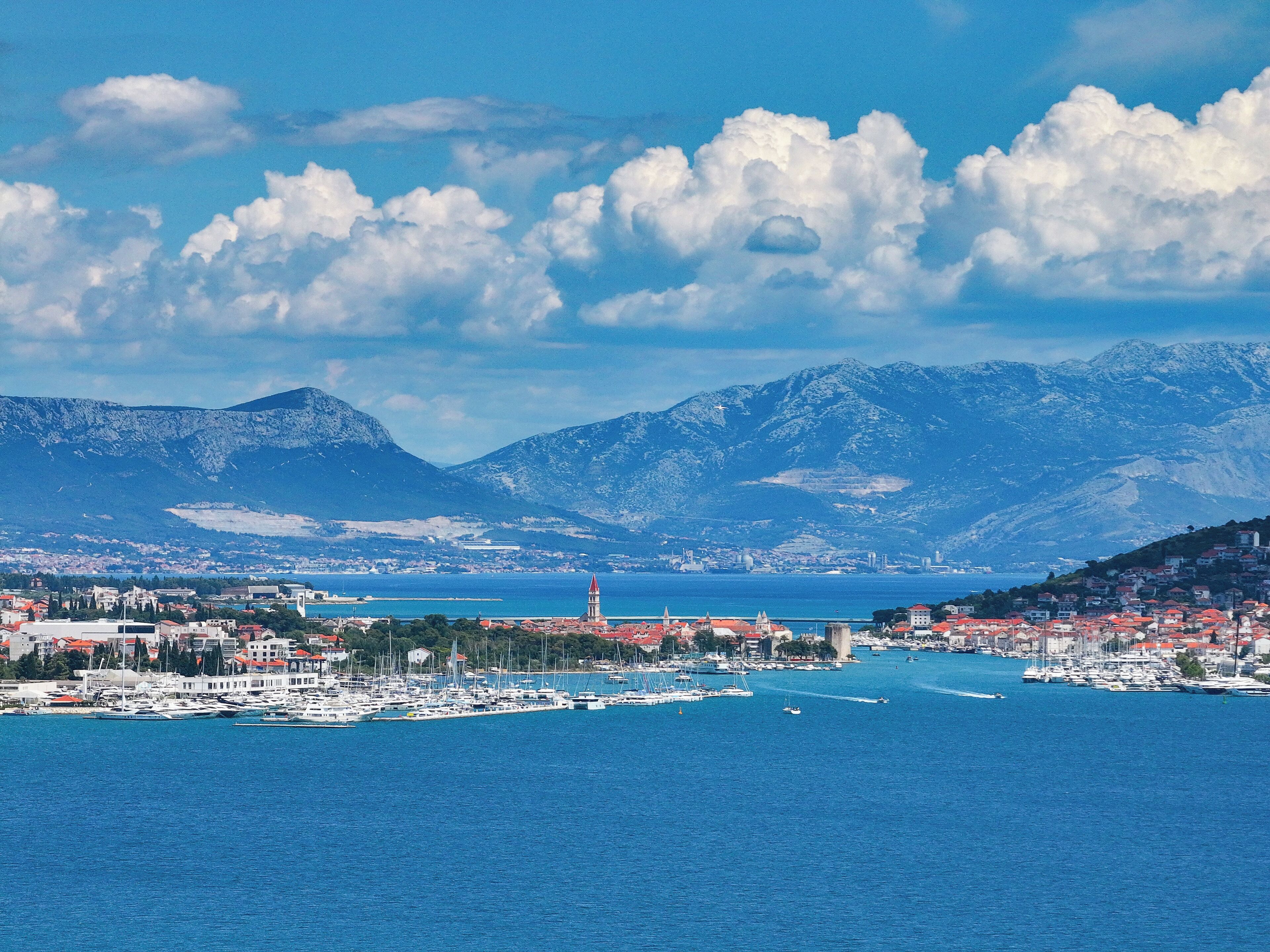A coastal town with a marina, mountains in the background, and a prominent tower.