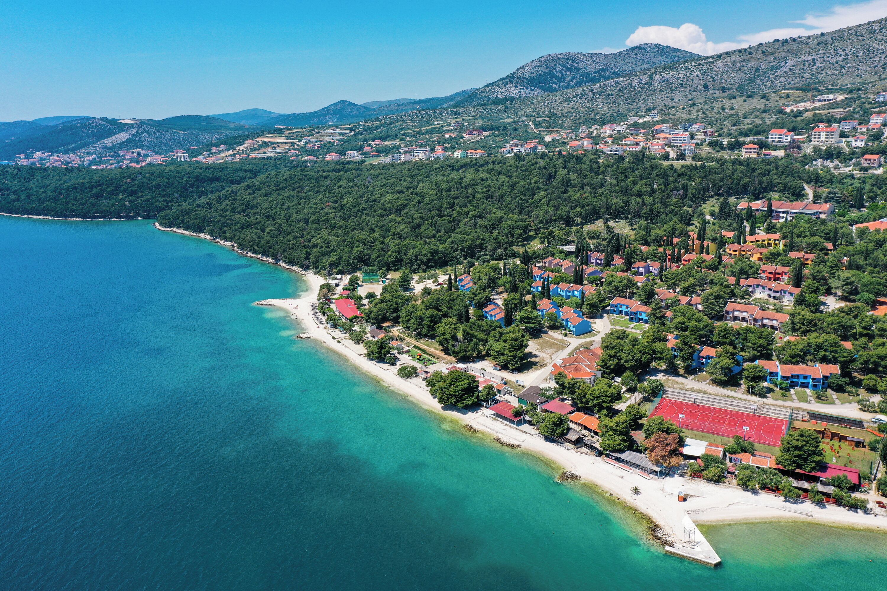 Vue aérienne d’une ville côtière avec une plage, des maisons et un court de tennis.