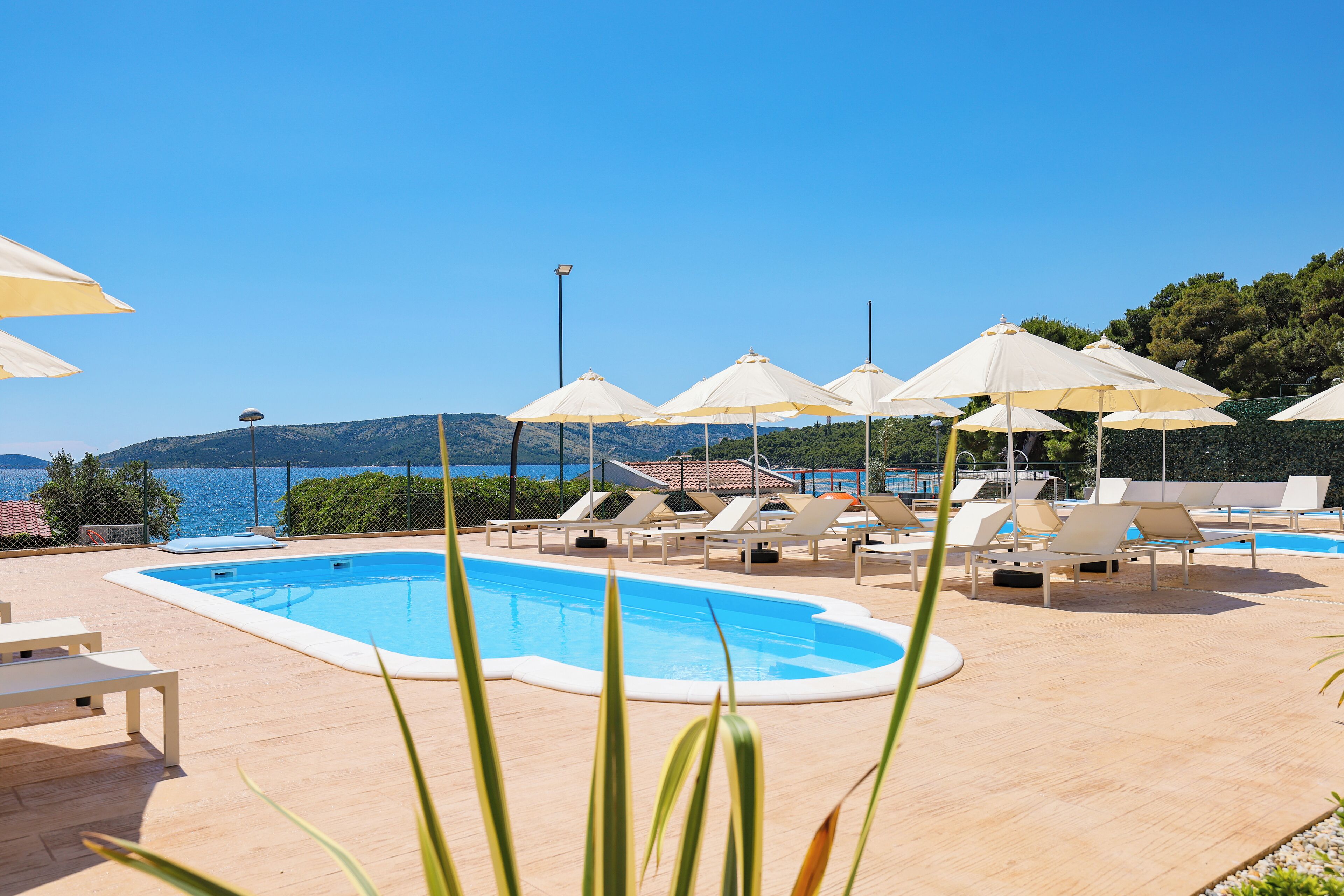 A pool area with lounge chairs and umbrellas, overlooking a body of water and hills.