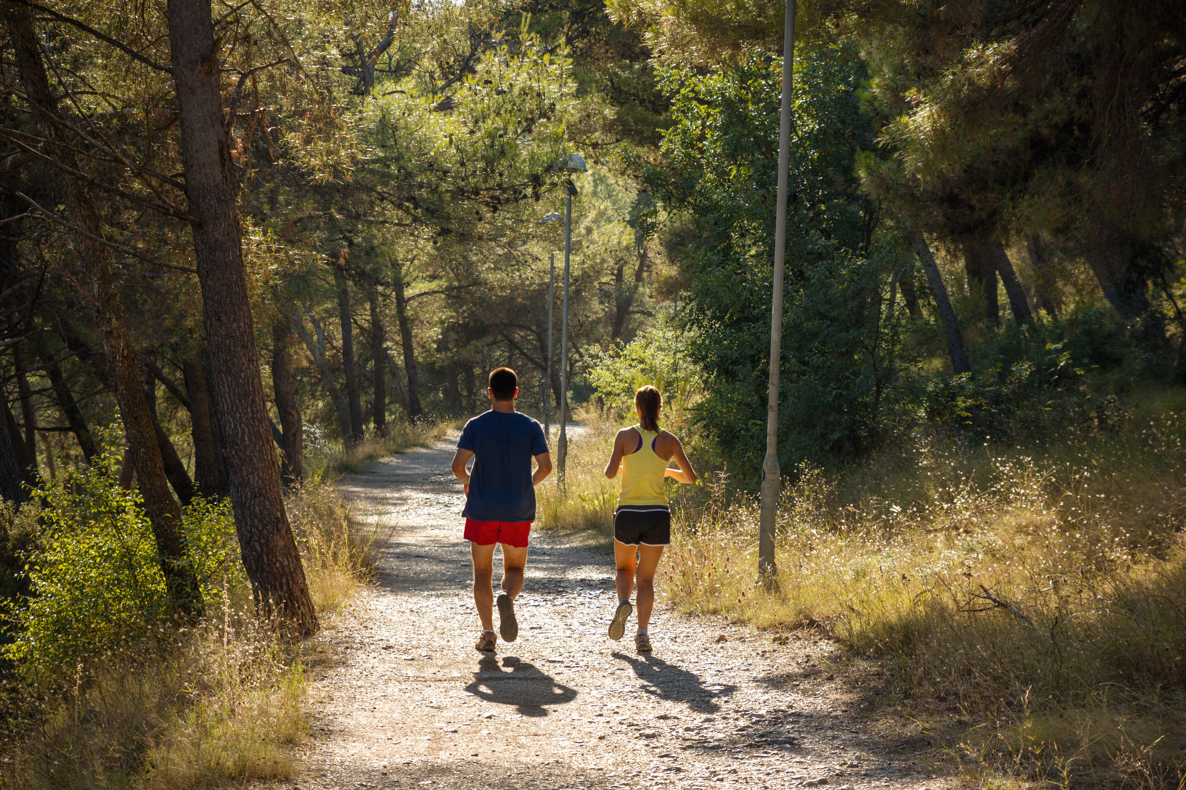 Two people running on a dirt path surrounded by trees.