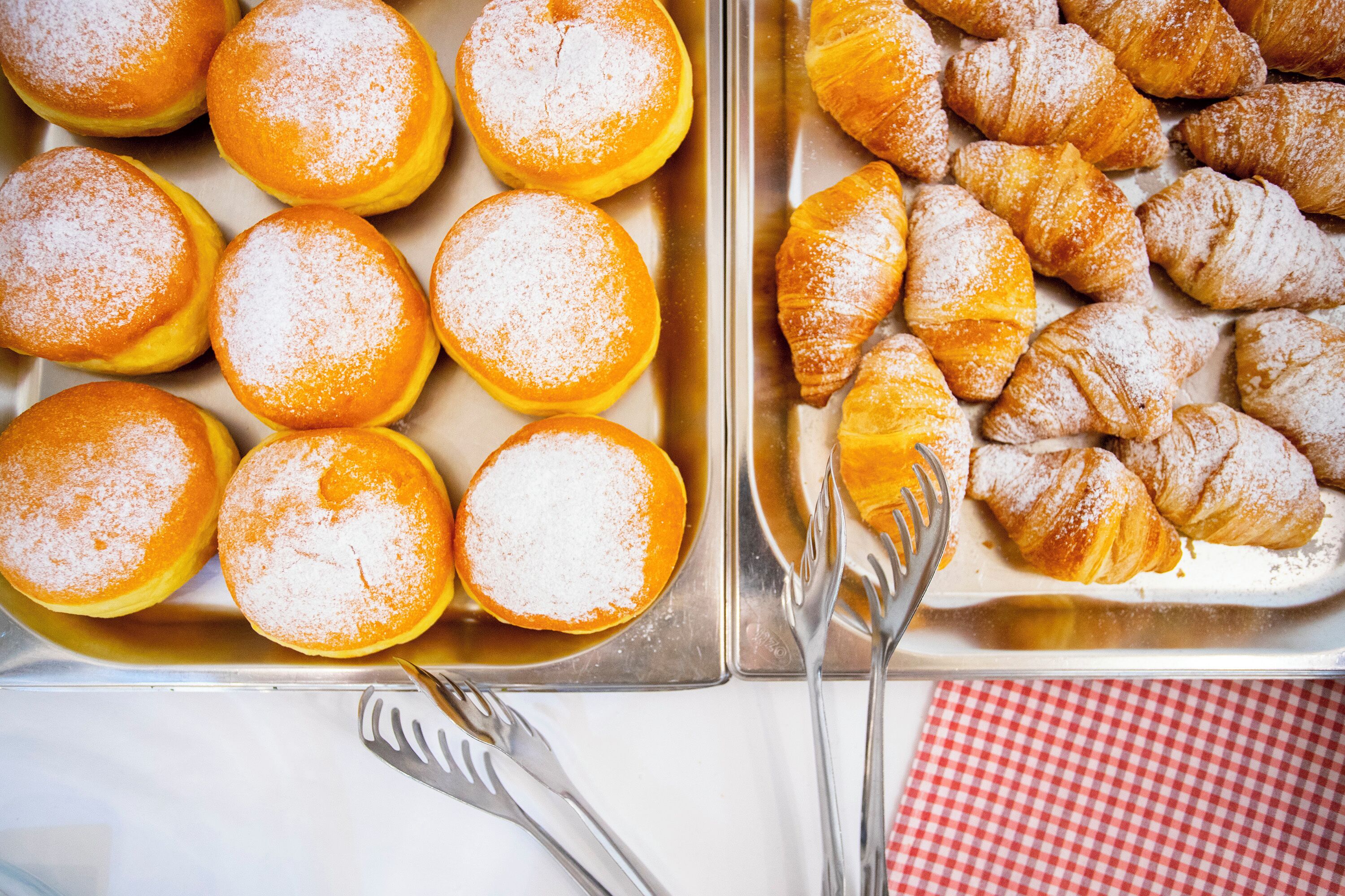 A tray of pastries, including donuts and croissants, on a table with a checkered napkin and silverware.