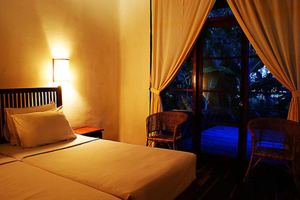 Habitación de hotel con cama, dos sillas, una mesita de noche y una ventana con cortinas.