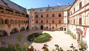 A courtyard with a central garden, surrounded by buildings with arched windows and a tower. - Jenbacherhof (Jenbach)