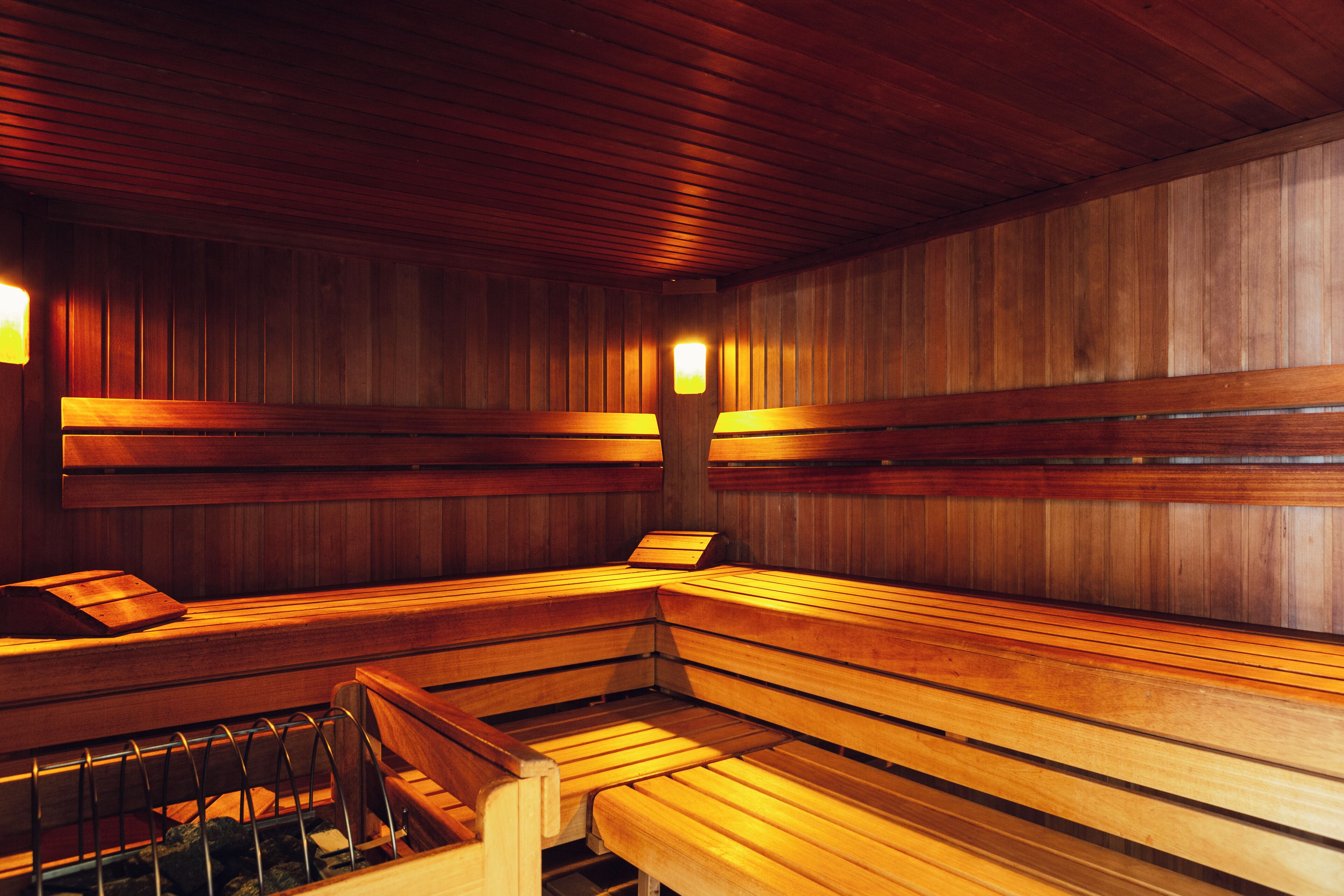 A sauna with wooden benches and walls, equipped with wall-mounted benches and a bench with a metal rack.