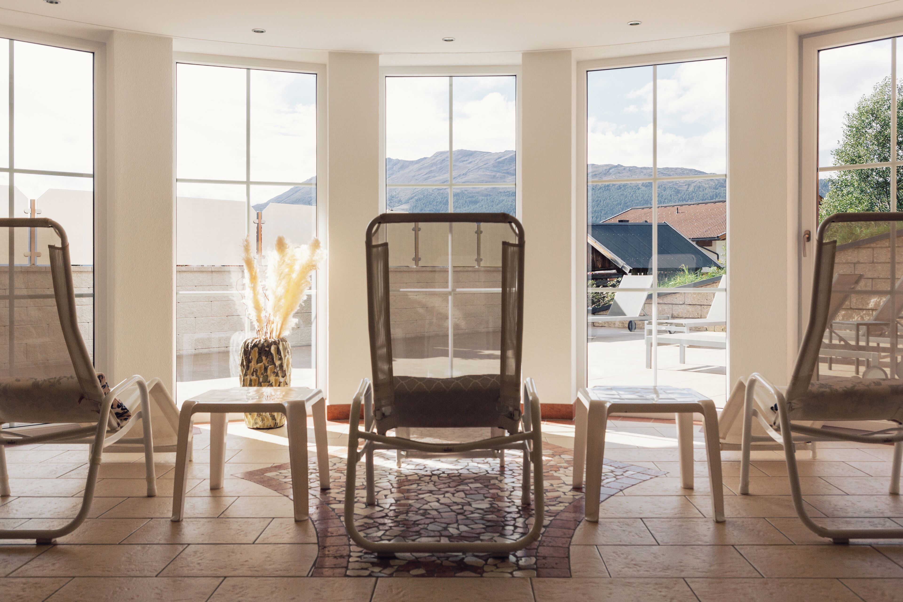 A room with large windows, a stone-tiled floor, and two lounge chairs.