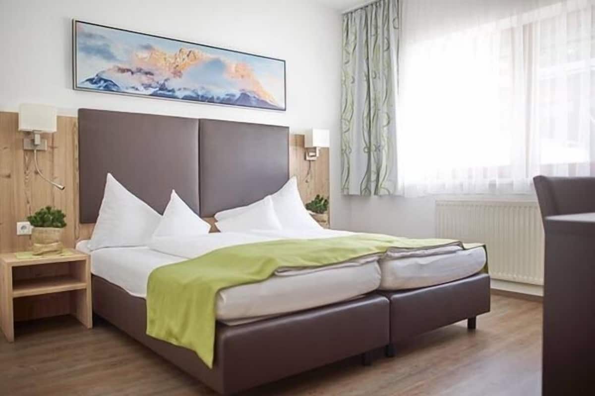 A modern hotel room with a large bed, a bedside table, a lamp, and a painting on the wall.