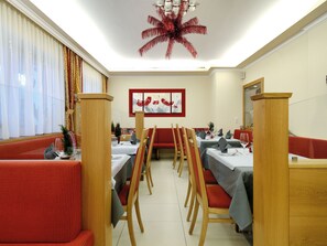 A restaurant with red upholstered booths, wooden chairs, and tables set for dining. - Hotel Venetblick (Jerzens)