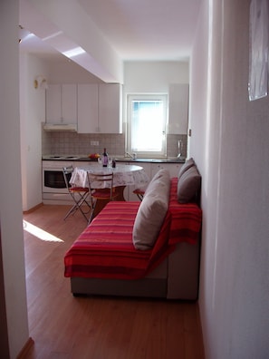 Un espacio habitable compacto con kitchenette, zona de comedor y sofá con manta a rayas marrones y rojas.