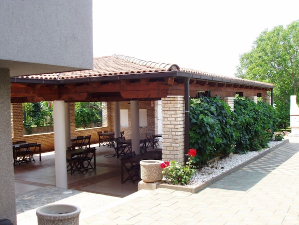 Un patio al aire libre con muros de ladrillo, techo de baldosas y varias mesas y sillas.