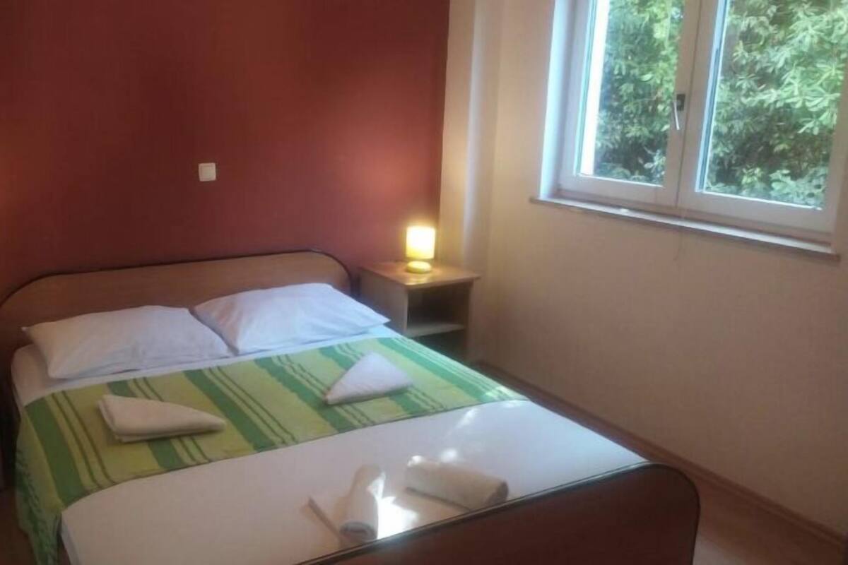 Un lit simple avec une couvre-lit à rayures vertes et blanches, deux oreillers blancs et une serviette pliée posée sur le lit. Il y a deux tables de chevet avec des lampes, une de chaque côté du lit.