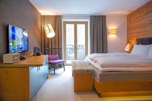 Habitación de hotel con cama, escritorio con televisor, silla, banco y puerta de vidrio corredera al exterior.