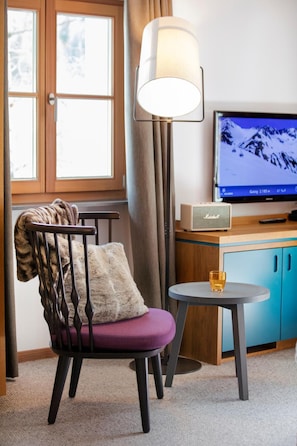 Una habitación con una silla, una lámpara, un televisor y una mesita con un vaso.