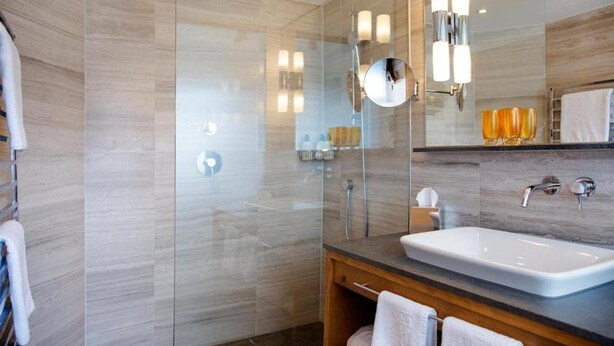 Un baño moderno con ducha de vidrio, un espejo grande y un lavamanos blanco.