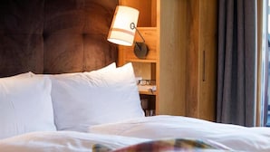 A bed with white linens, a brown headboard, a bedside lamp, and a wooden shelf with glasses. - Valluga (Sankt Anton am Arlberg)
