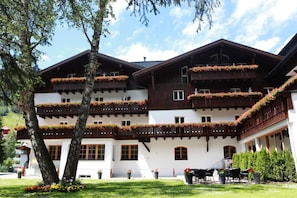 A multi-story building with balconies adorned with flowers, a well-maintained lawn, and outdoor seating. - Valluga (Sankt Anton am Arlberg)