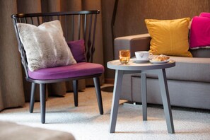 A modern living room with a grey sofa, a black chair with a purple cushion, and a small round table with a cup and a croissant. - Valluga (Sankt Anton am Arlberg)