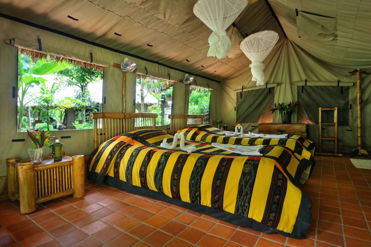 A room with a large bed, a small table, and a window with a view of greenery.