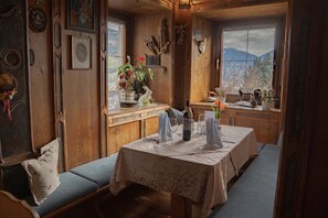 A cozy dining area with a wooden table set for two, a bench, and a view of mountains through the window. - Hotel Gasthof Gribelehof (Lienz)